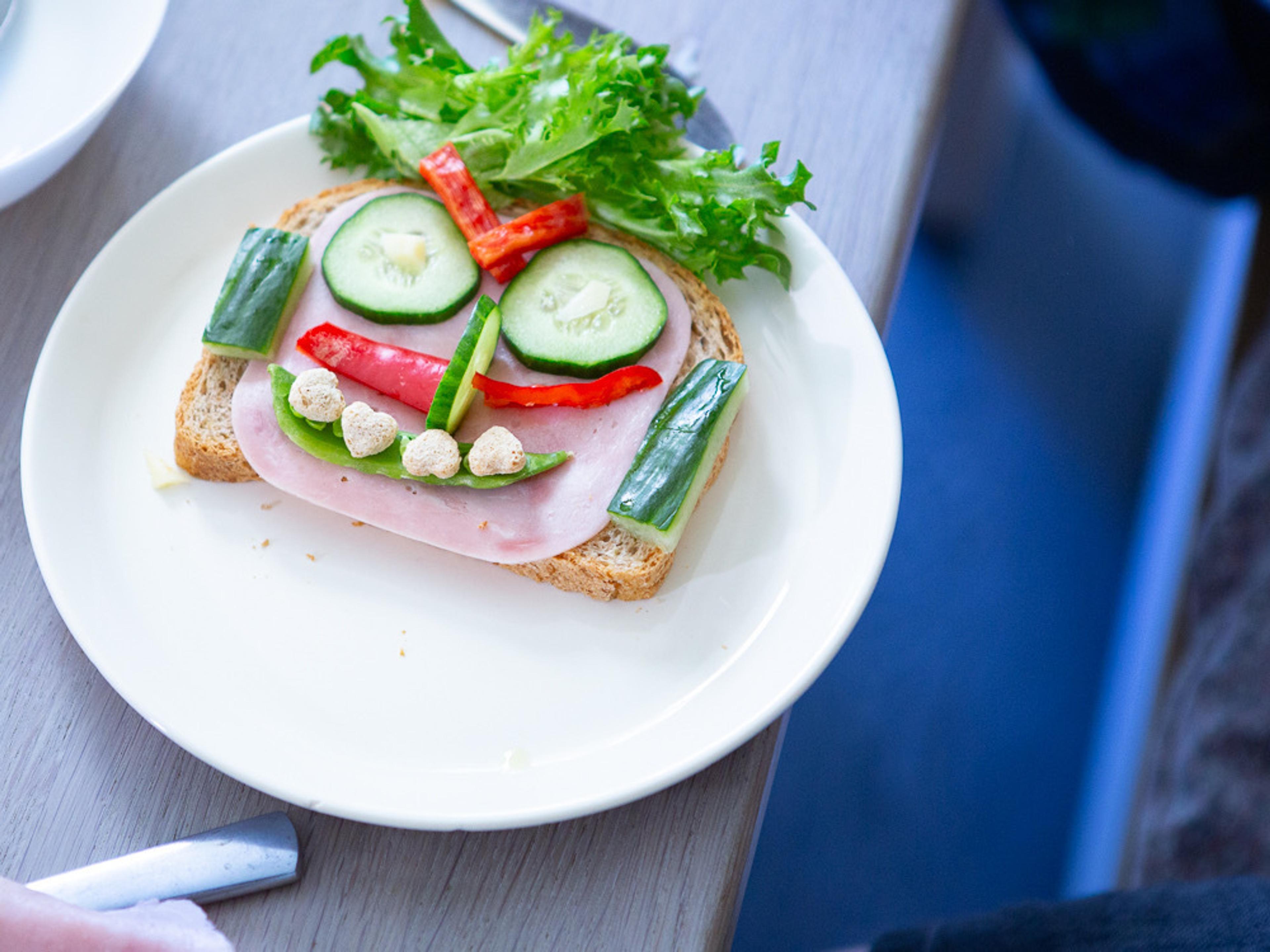 Bilde av brødskive med skinke, øyne av agurker, munn av sukkerert og hår av salat