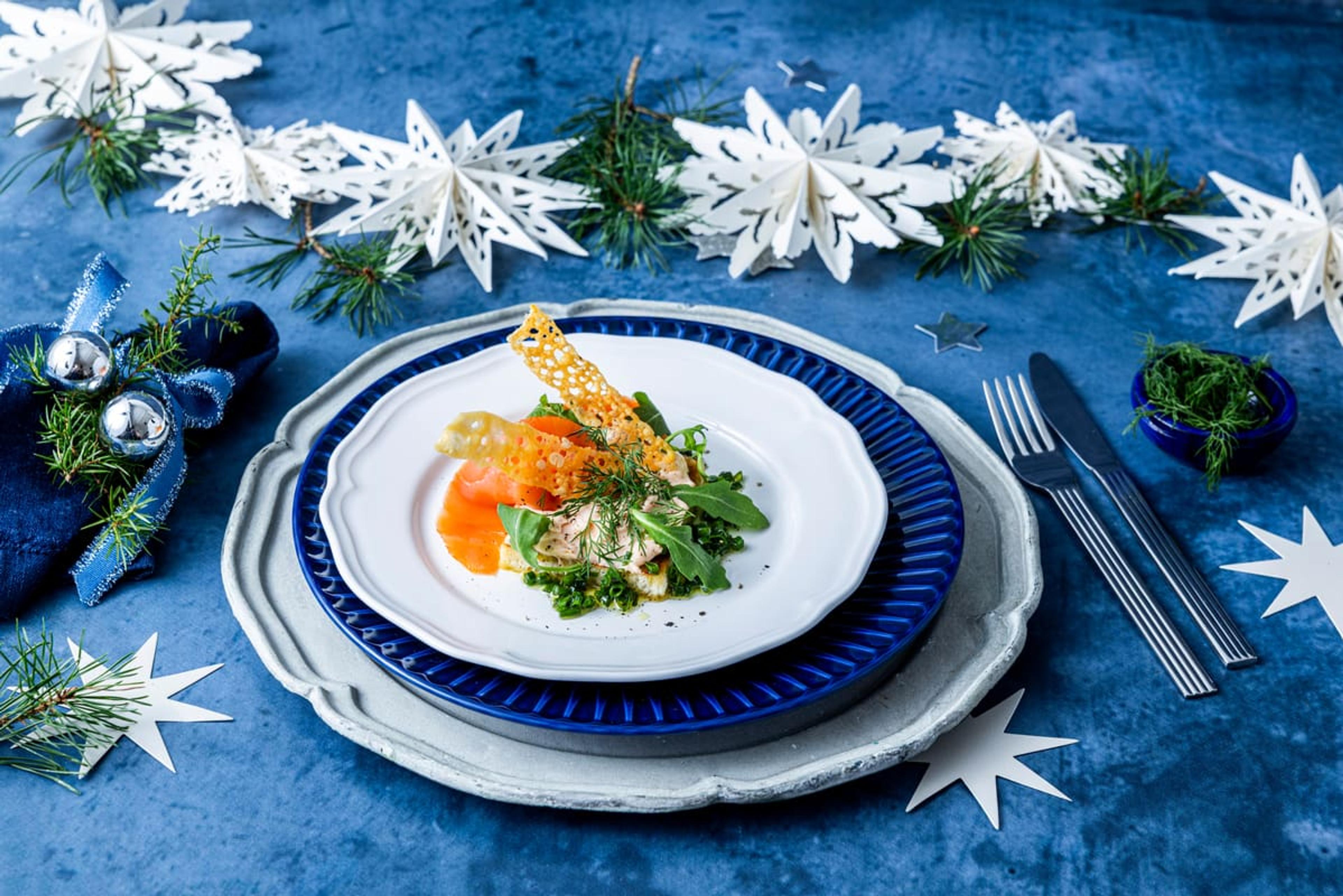 Forrett med røkelaks, grønt og sprø osteservert på dekorativ tallerken med julepynt.