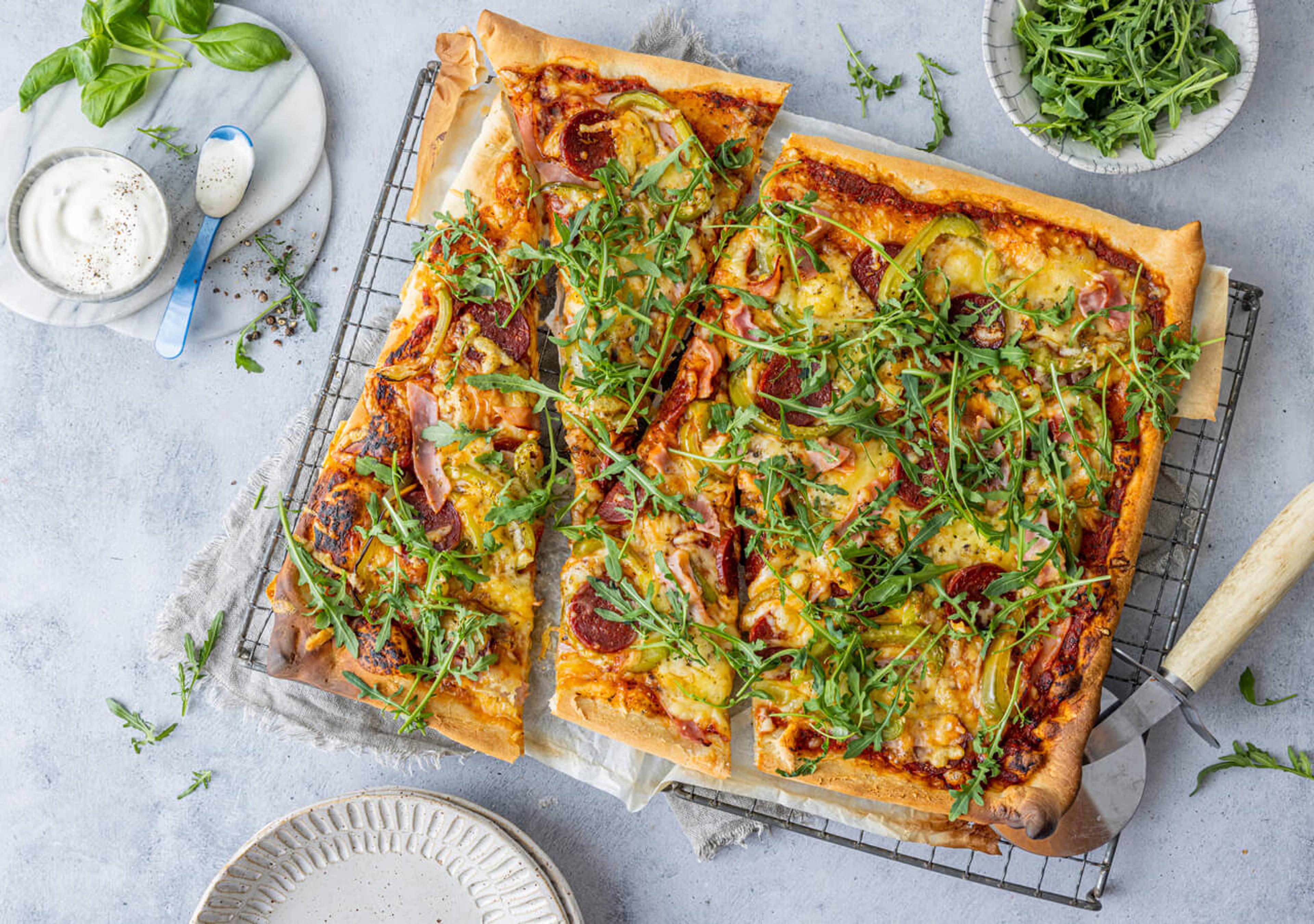Hjemmelaget pizza med ost, skinke, pepperoni, paprika og ruccula. Servers med hvit pizzadressing.