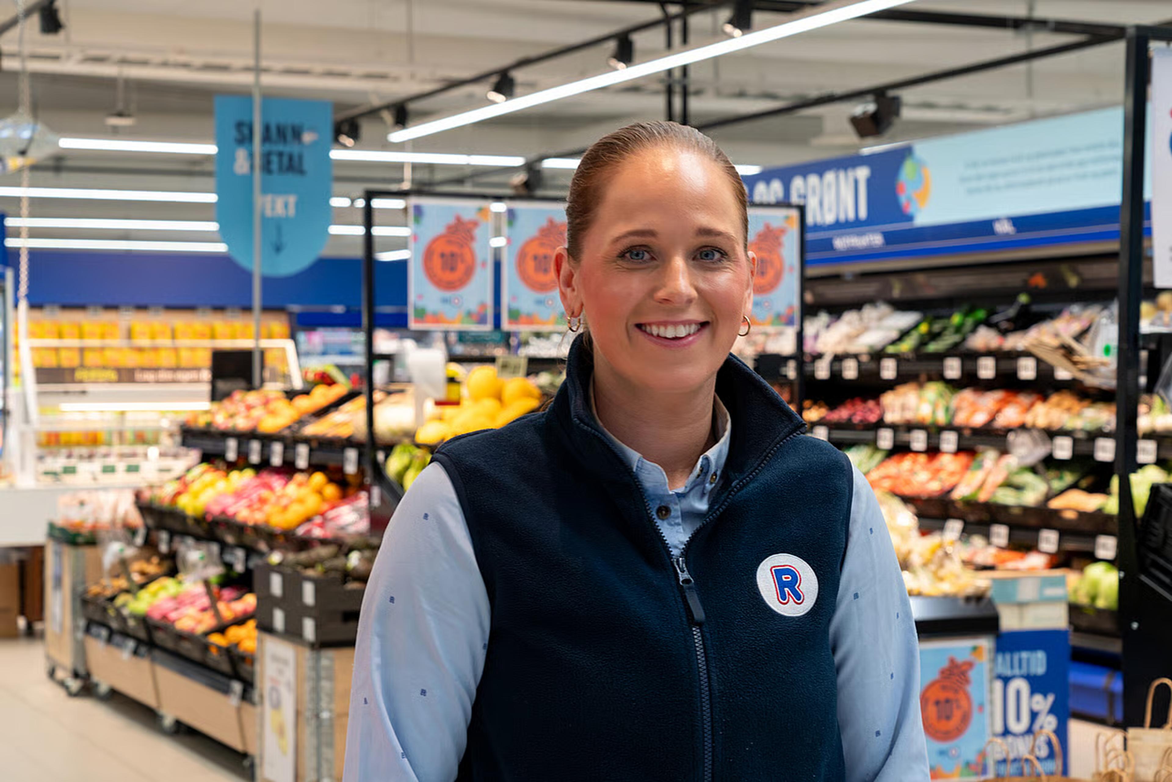 REMA-ansatt "Signora" smiler i uniformen sin foran frukt og grønt-avdelingen