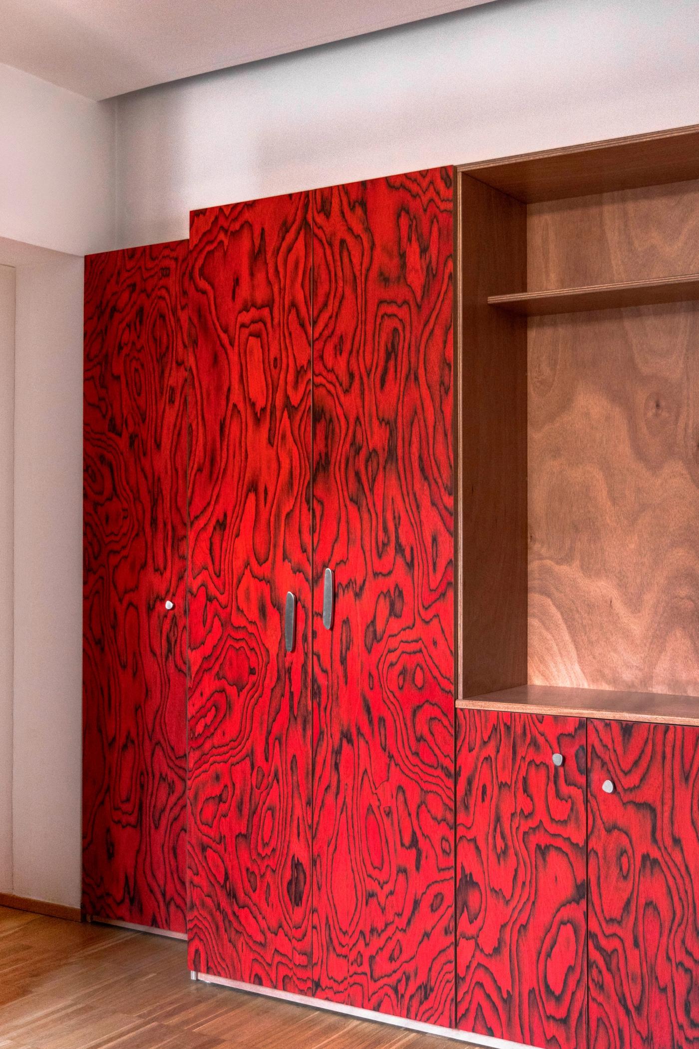 Armadio su misura rosso con motivi decorativi e ripiani in legno naturale integrato in parete.