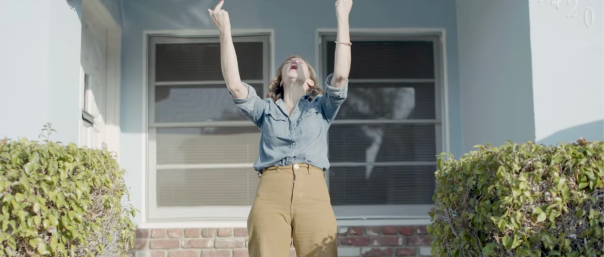 Woman standing outside her home with her middle fingers raised to the sky 