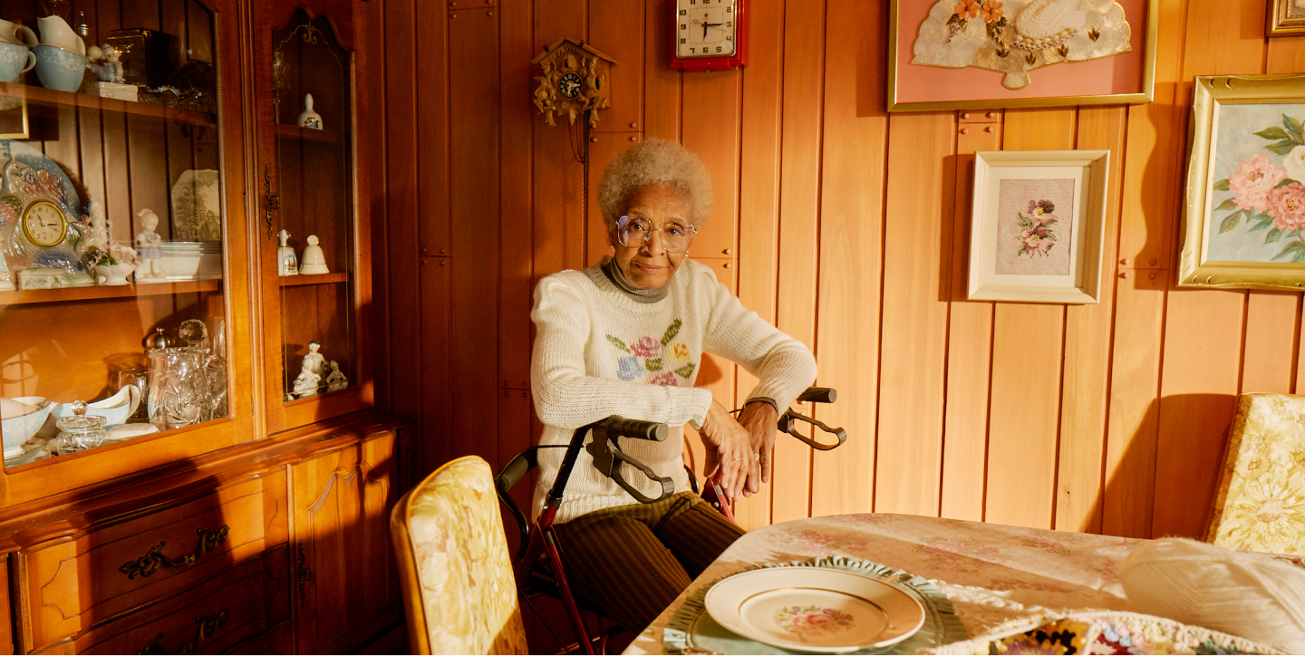 A woman sits waiting in her dining room, with an empty plate on the table. 