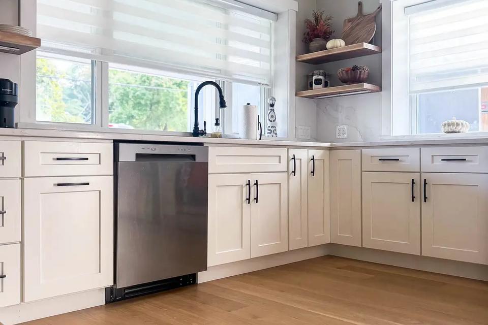 White kitchen cabinets, a stainless steel dishwasher and black sink beneath two windows