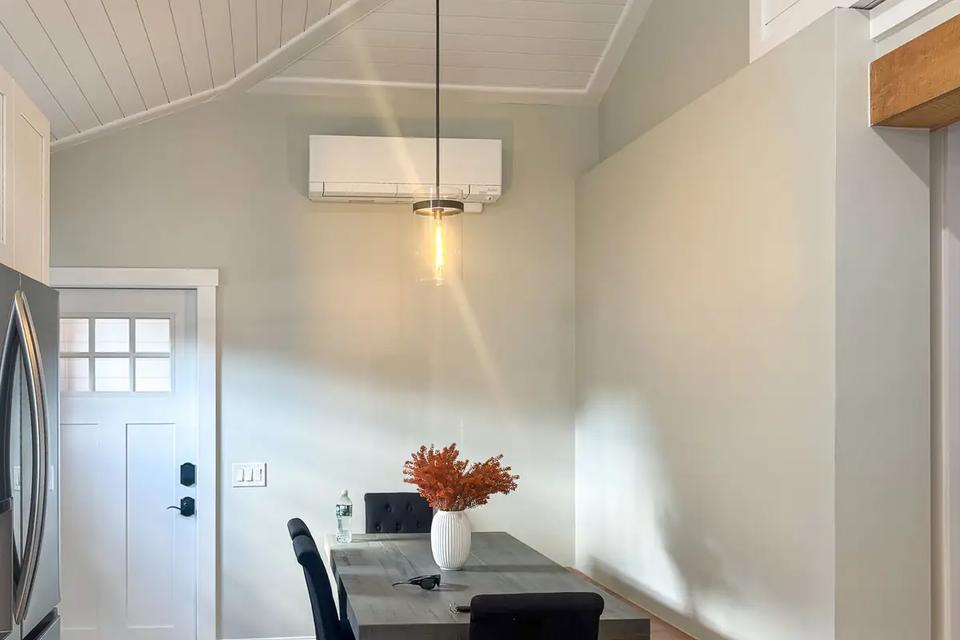 Dining table and chairs beside a built-in bench under a vaulted white plank ceiling