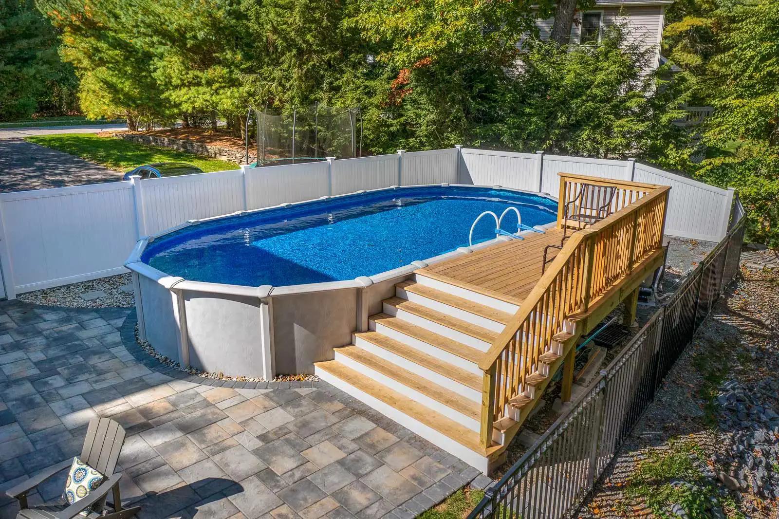 Above-ground pool with a completed wood deck, broad staircase and surrounding stone patio