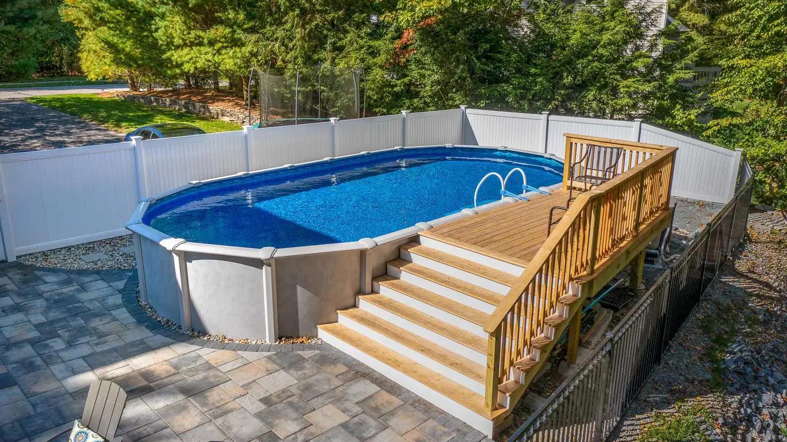 Above-ground pool with a completed wood deck, broad staircase and surrounding stone patio