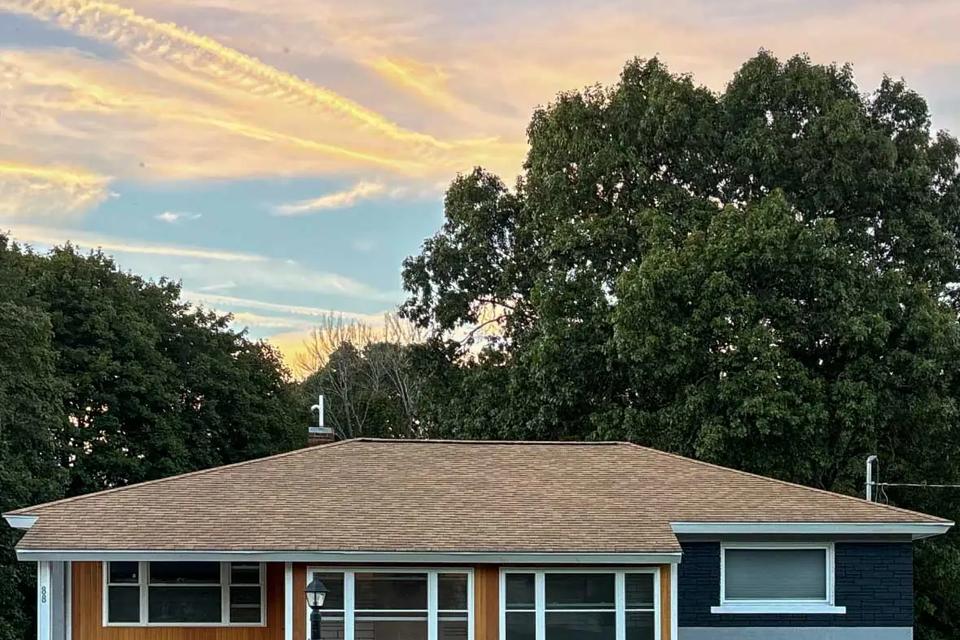 Single-story home with warm cedar siding, white-trimmed windows and a front lawn at sunset