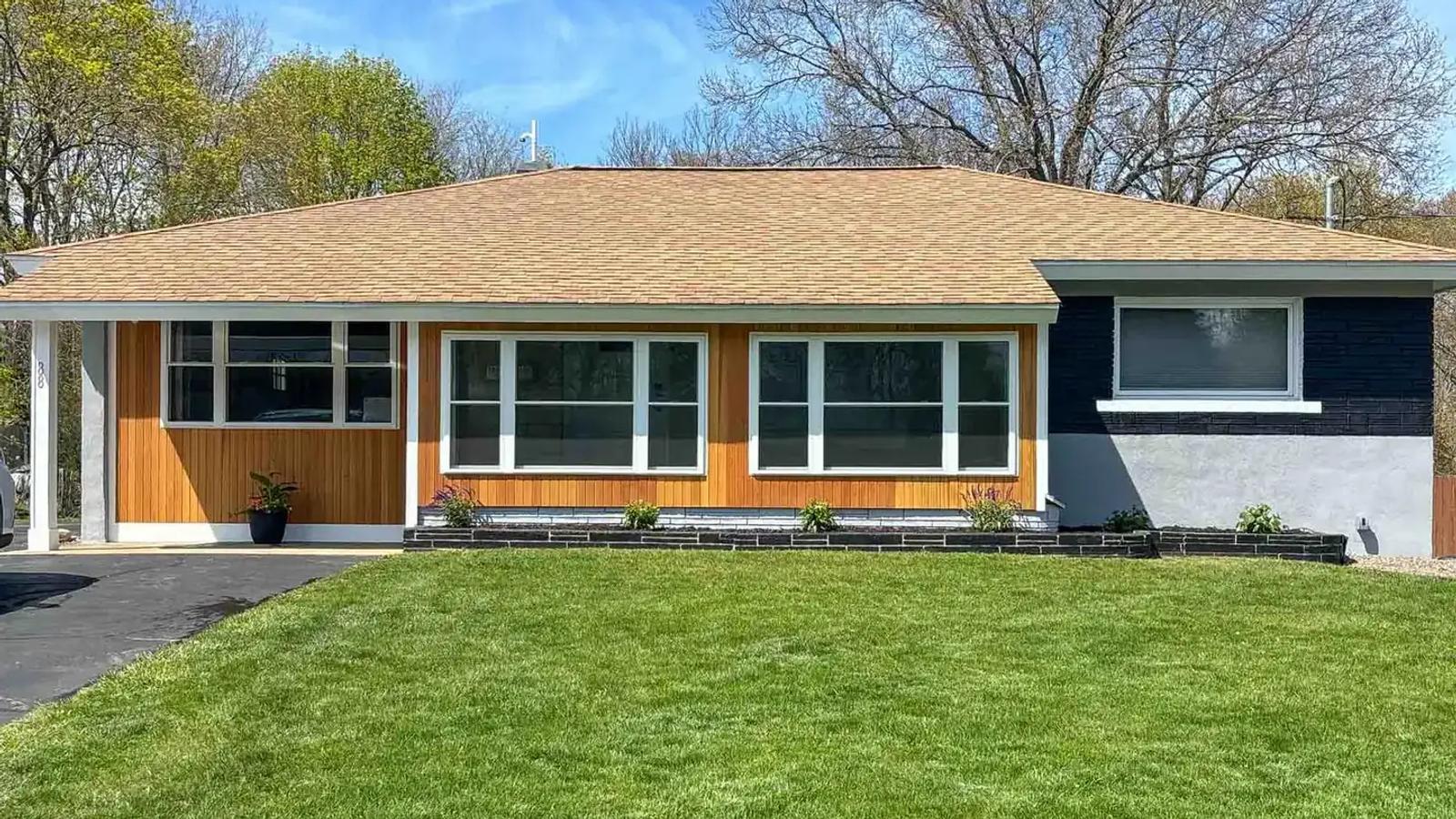 Single-story home with cedar siding, white-trimmed windows and a green front lawn