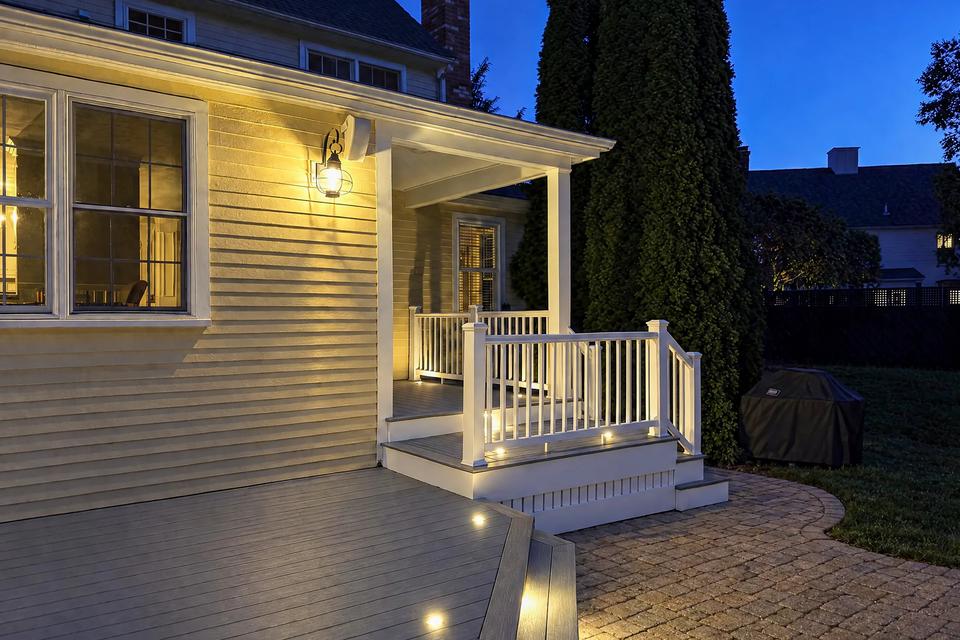 Illuminated side porch, white railings and curved paver landing at dusk