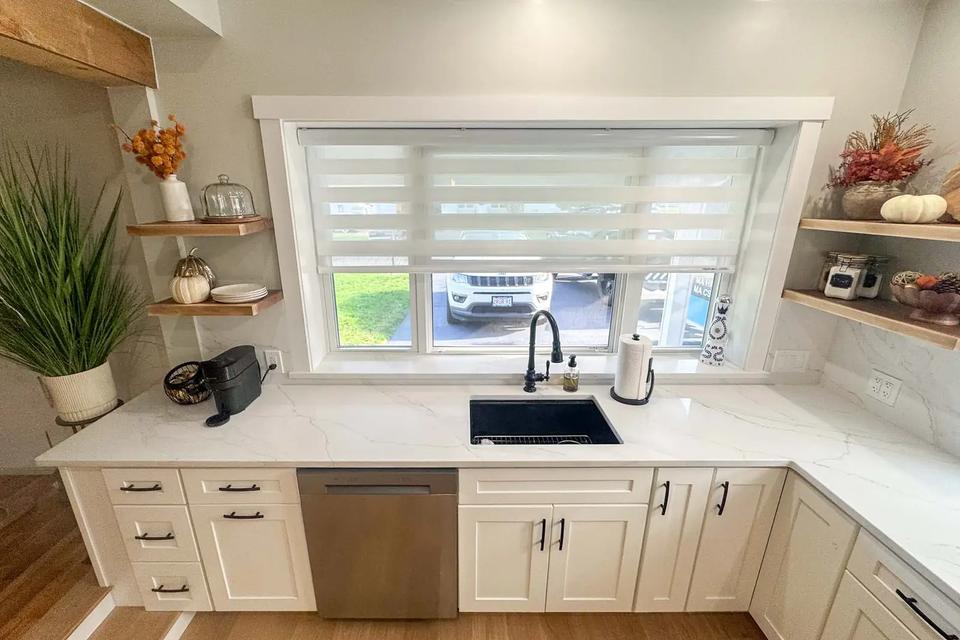 Elevated view of a black sink, white countertops, dishwasher and open corner shelves
