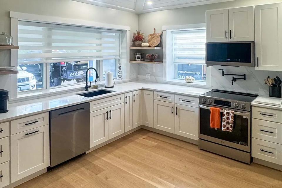White kitchen with stainless steel appliances, wood flooring and a vaulted plank ceiling