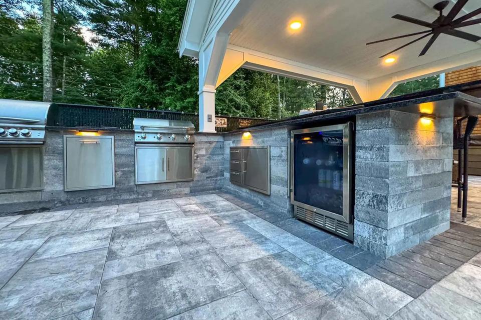 Stone-faced outdoor kitchen with stainless steel cabinets, grill and a glass-front beverage fridge