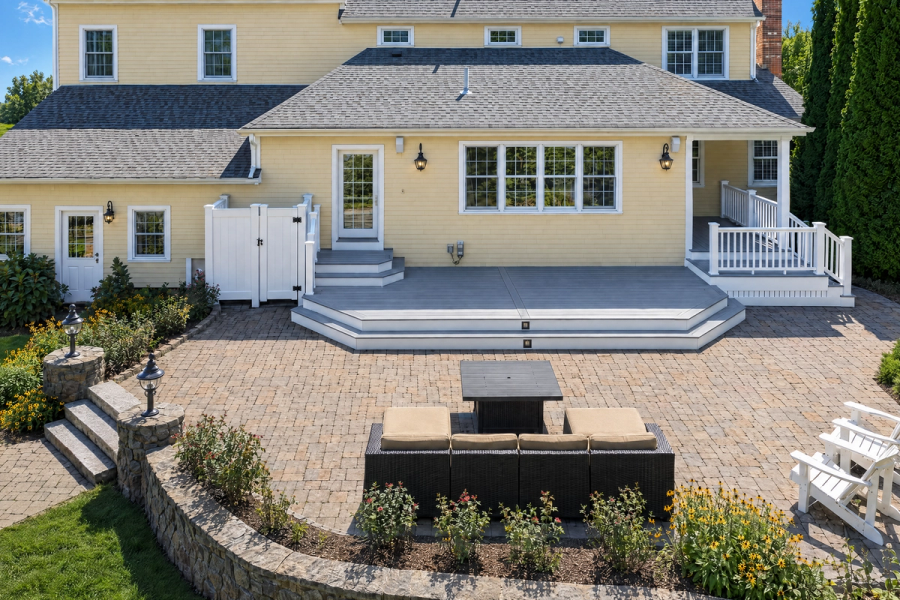 Elevated front view of a finished gray deck with wide steps and white railings behind a yellow home