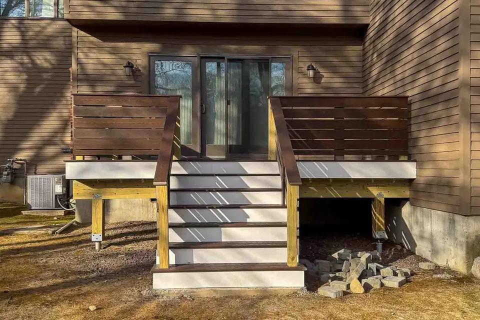 Straight-on view of grey deck stairs with dark railings leading to a sliding glass door