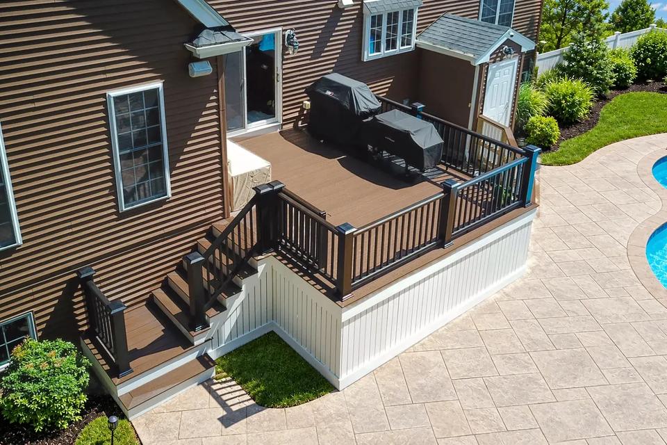Raised composite deck with black railings and stairs leading down to the pool patio