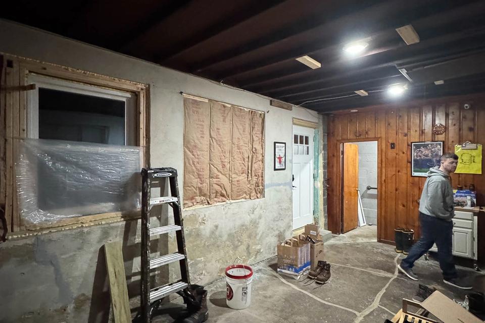 Wide view of the unfinished garage with exposed ceiling beams, tools and a worker
