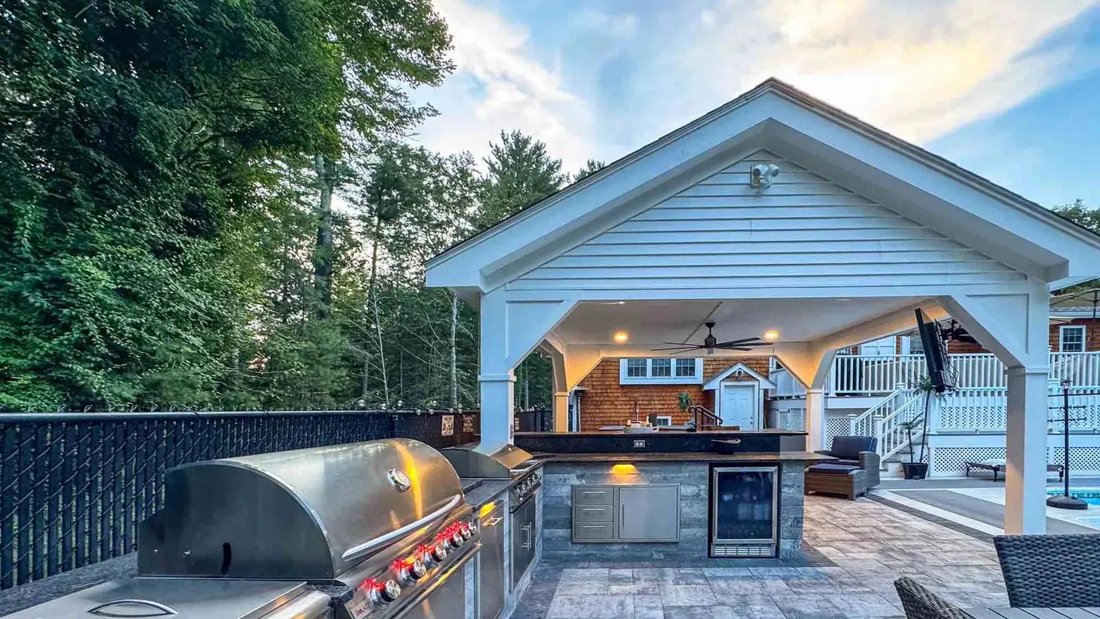 White pool pavilion at dusk with a built-in grill, outdoor kitchen and warm ceiling lights
