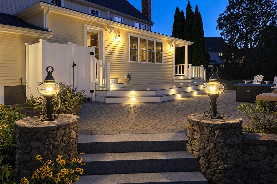 Backyard deck at dusk with warm integrated lighting and foreground garden lanterns