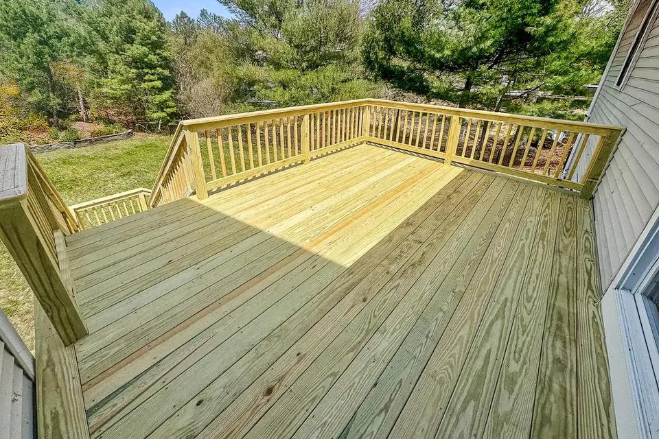 Wide view across the wood deck with vertical baluster railings and trees beyond