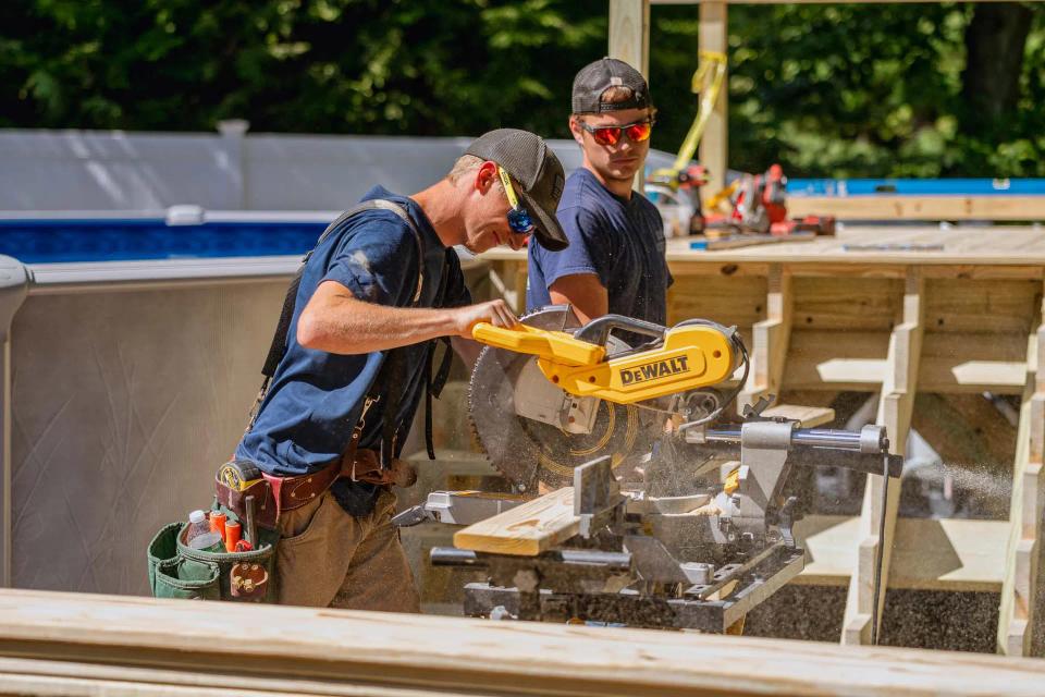 Two carpenters cutting deck lumber at a miter saw beside the pool