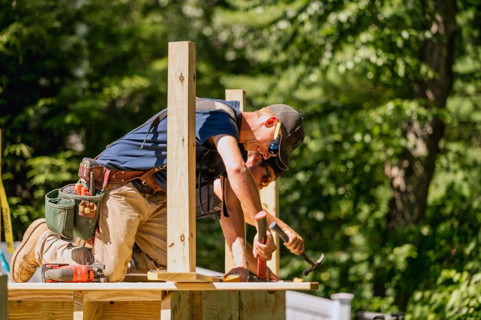 Carpenter kneeling beside a vertical post while securing a wood deck board