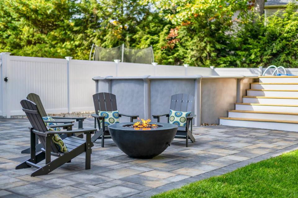 Adirondack chairs around a fire pit on the stone patio beside the pool stairs