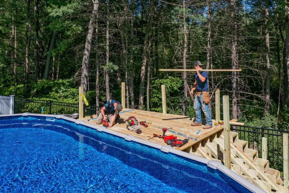 Carpenters working on the pool deck with upright posts and a long horizontal board
