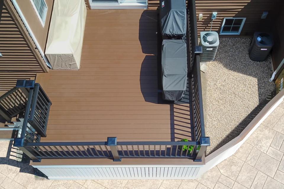 Overhead view of brown deck boards, black railings and covered grills beside the house