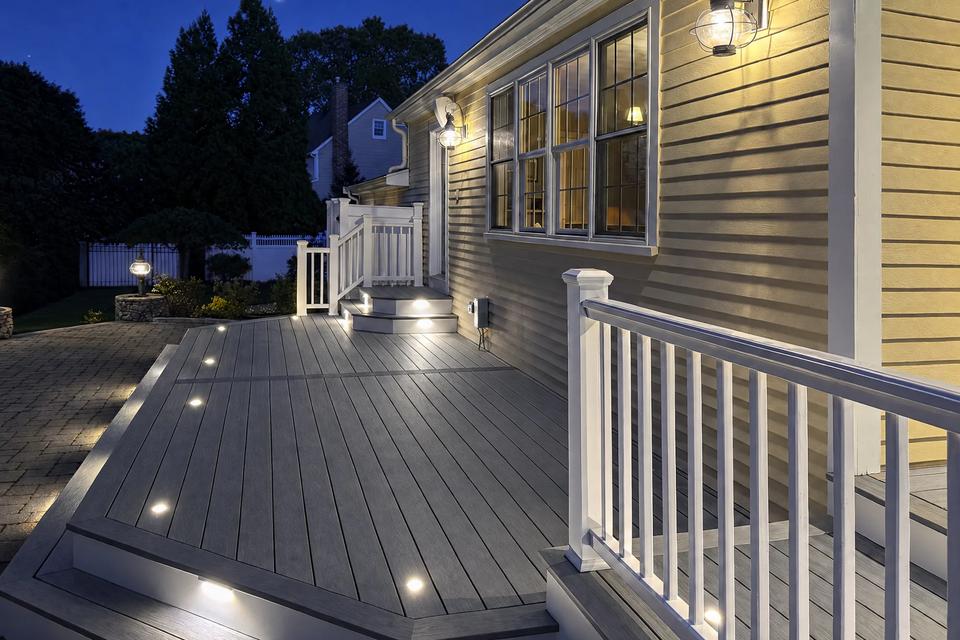 Nighttime view along the grey deck with recessed lighting and white railings
