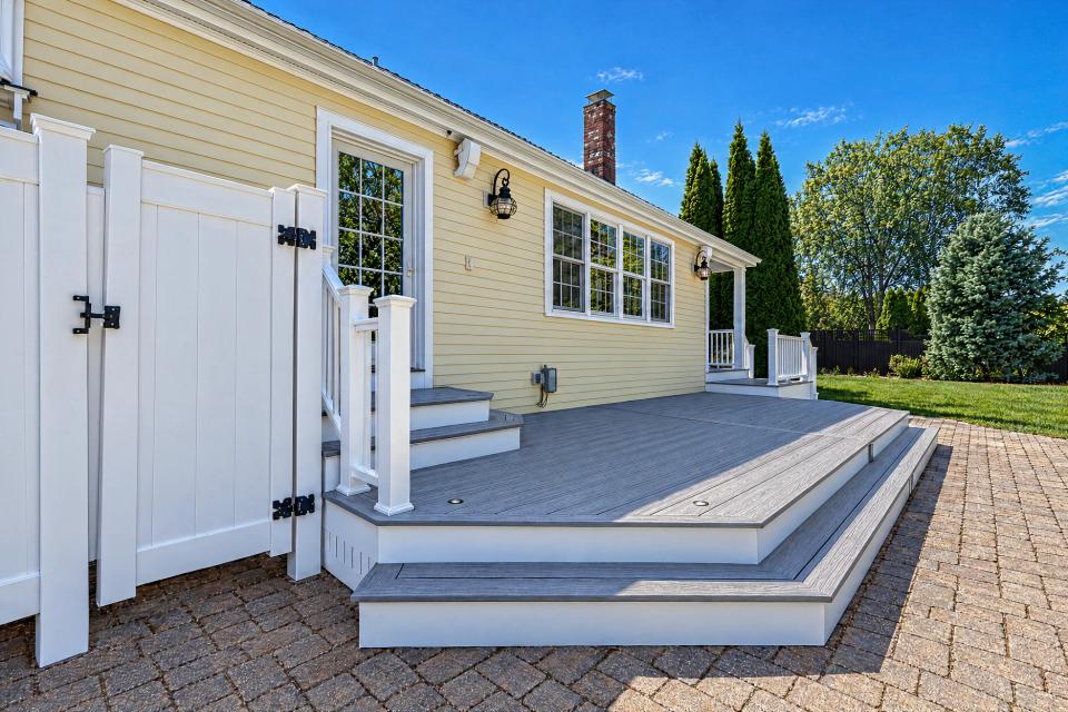 Close view of grey deck boards, wide steps and white trim beside the house