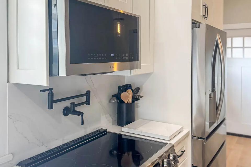 Stainless steel range and microwave with white cabinetry and a black pot filler