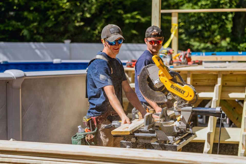 Two carpenters standing at a miter saw with the pool deck under construction behind them