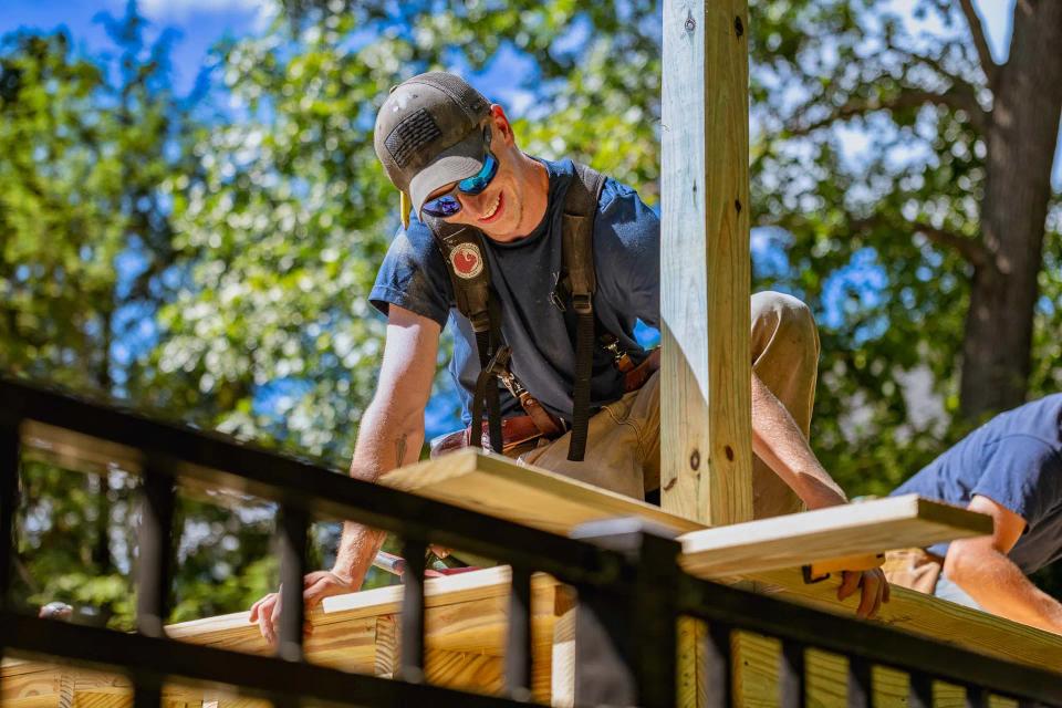 Carpenter kneeling on the deck while fitting wood boards beside a railing post