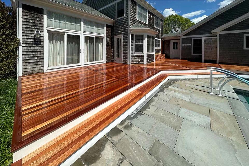 Long mahogany deck and white trim along the stone pool patio beside the house