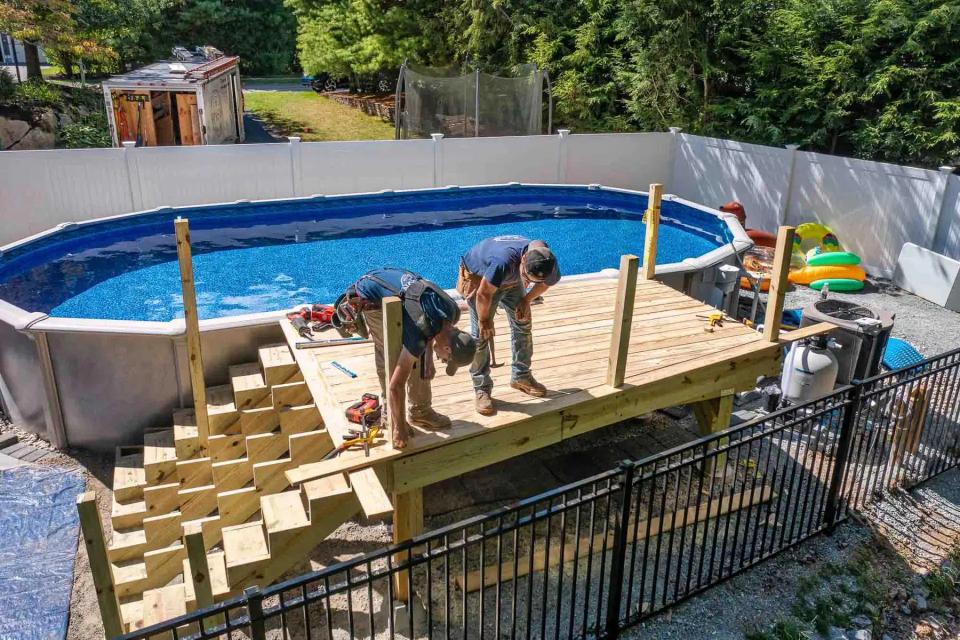 Elevated view of two carpenters working on the deck beside the pool and unfinished stairs