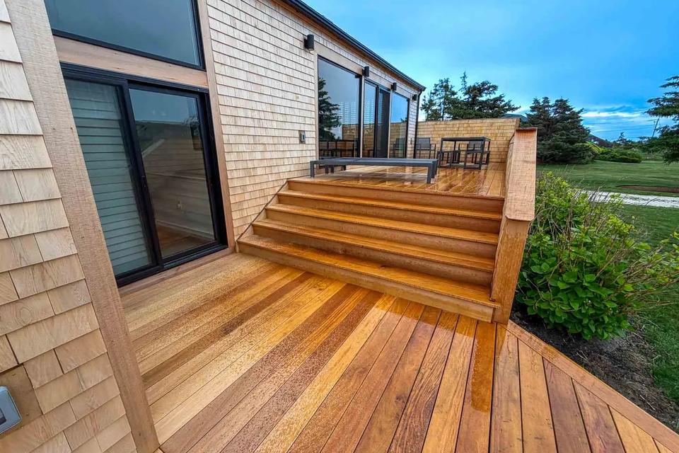 Wide Garapa stairs connecting two deck levels beside the cedar-shingled home