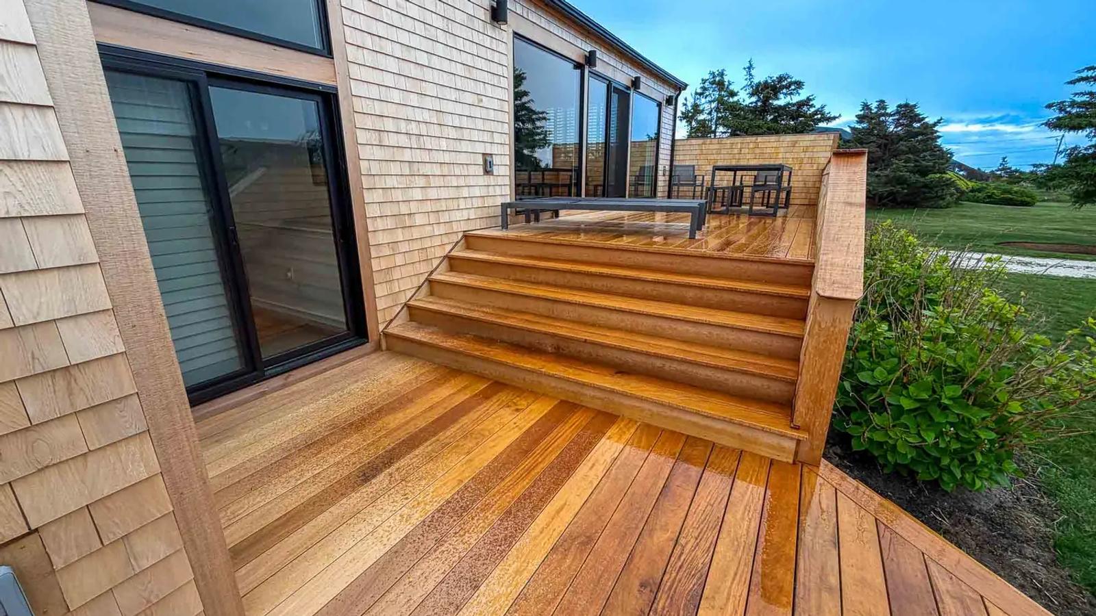 Wide Garapa stairs connecting two deck levels beside a cedar-shingled home