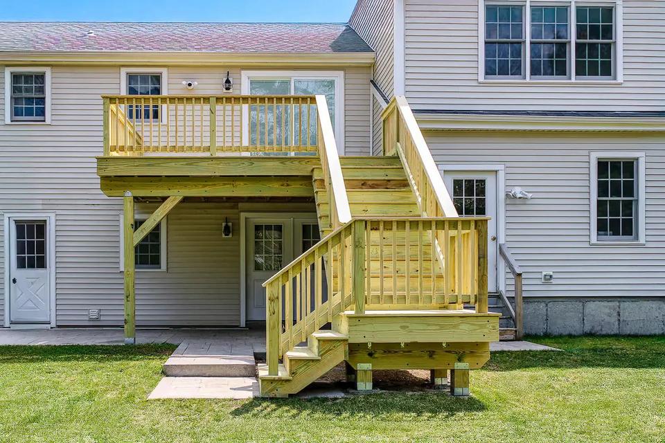 Wood stairs descend from the upper deck to a square landing above the lawn