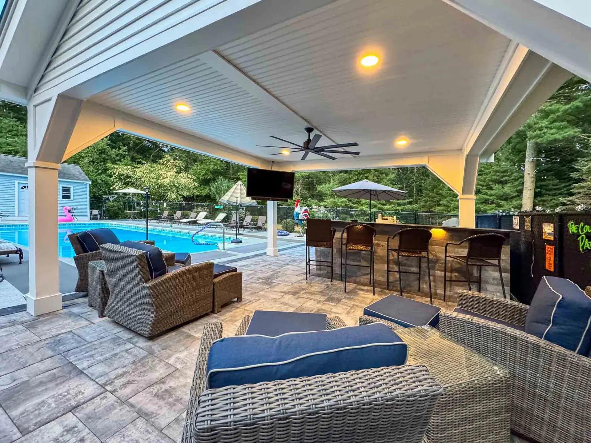Wicker seating and a bar beneath the pavilion ceiling with recessed lights and a ceiling fan