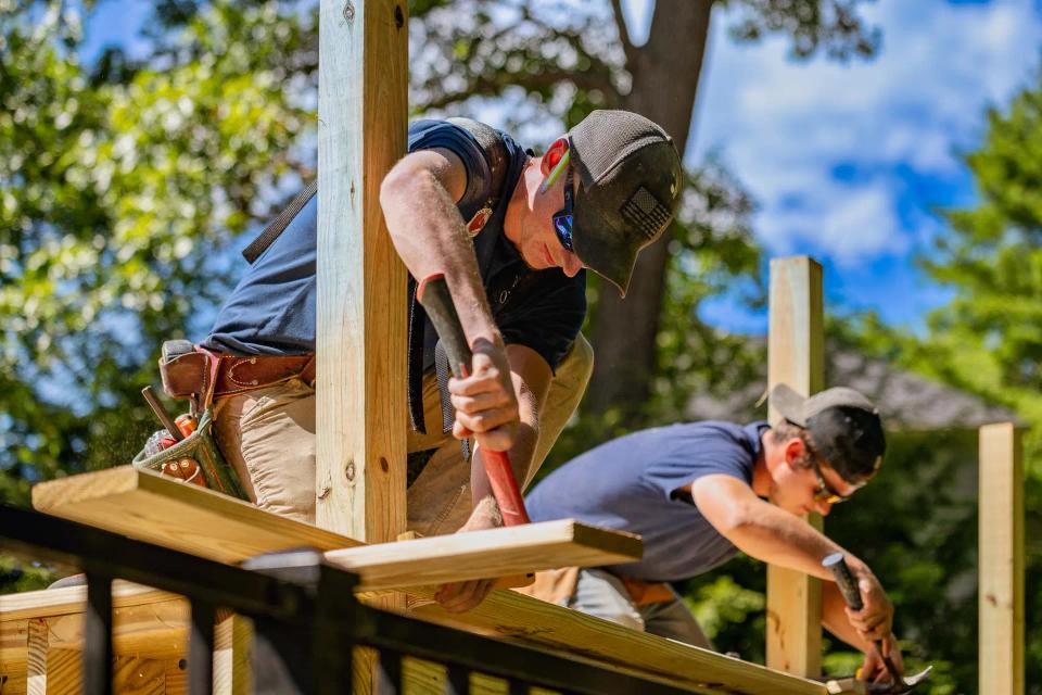 Close view of two carpenters working on deck boards between upright railing posts