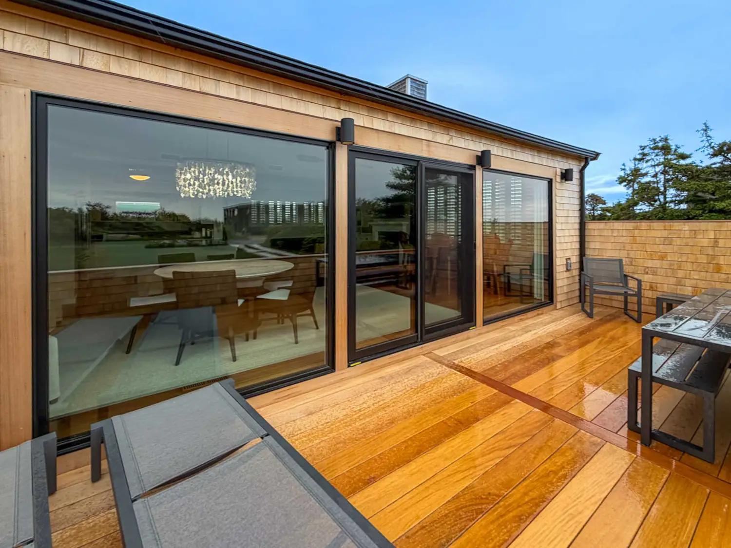 Garapa terrace with lounge chairs and a dining table outside black-framed glass doors