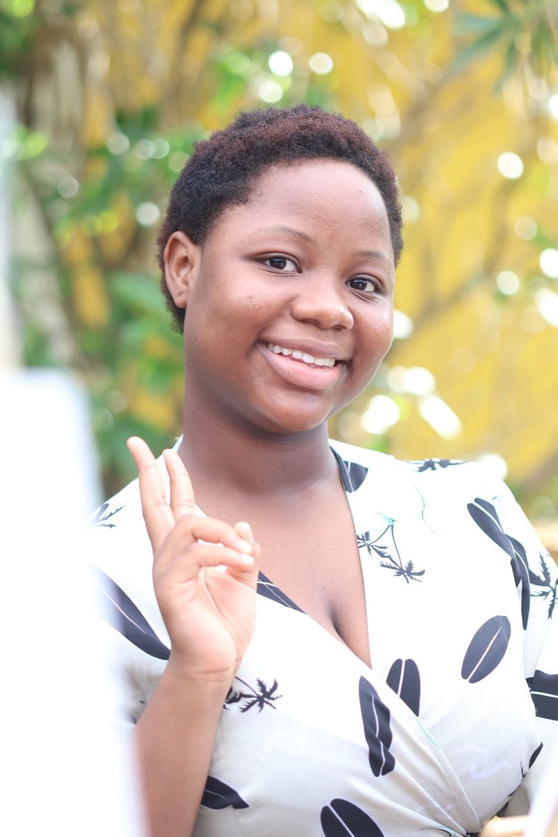 A smiling young woman in a leaf-print dress makes a peace sign at the book club gathering