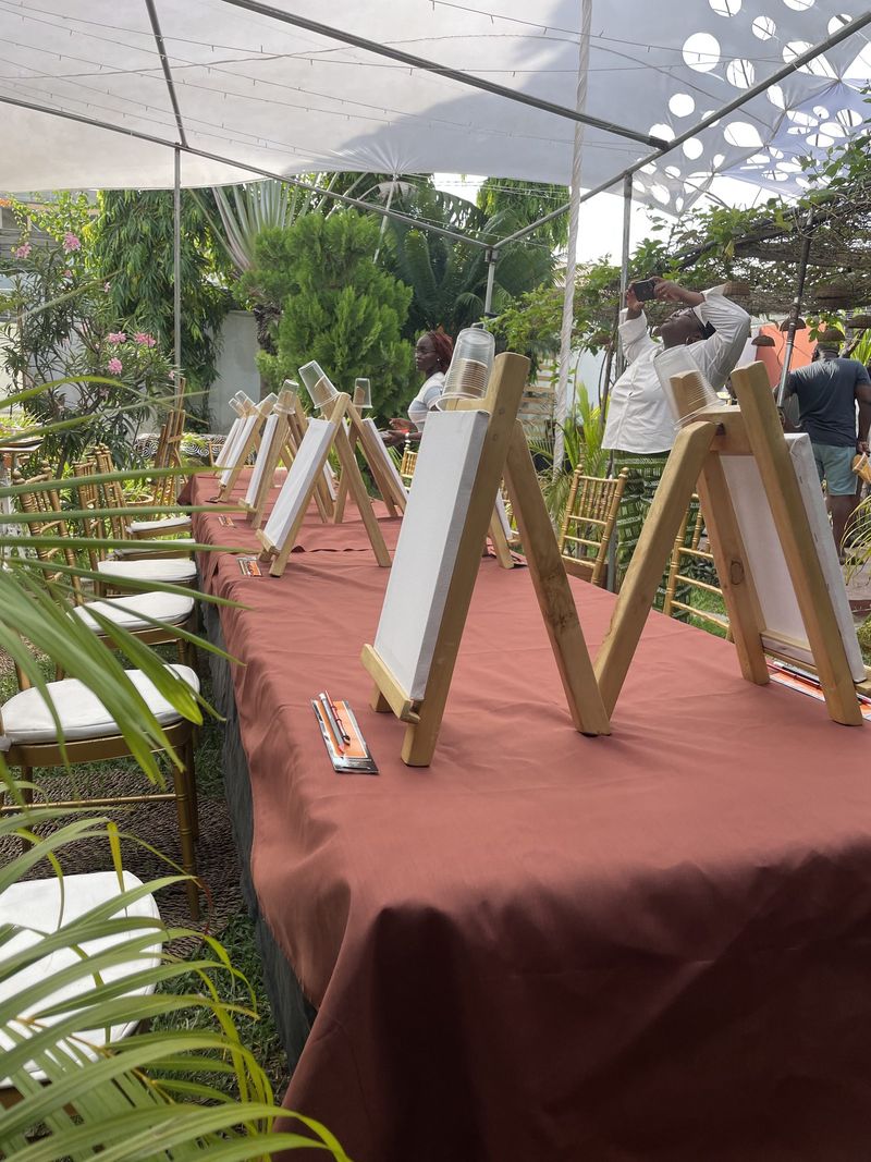 A long table set with rows of easels and blank canvases under a garden marquee before the workshop