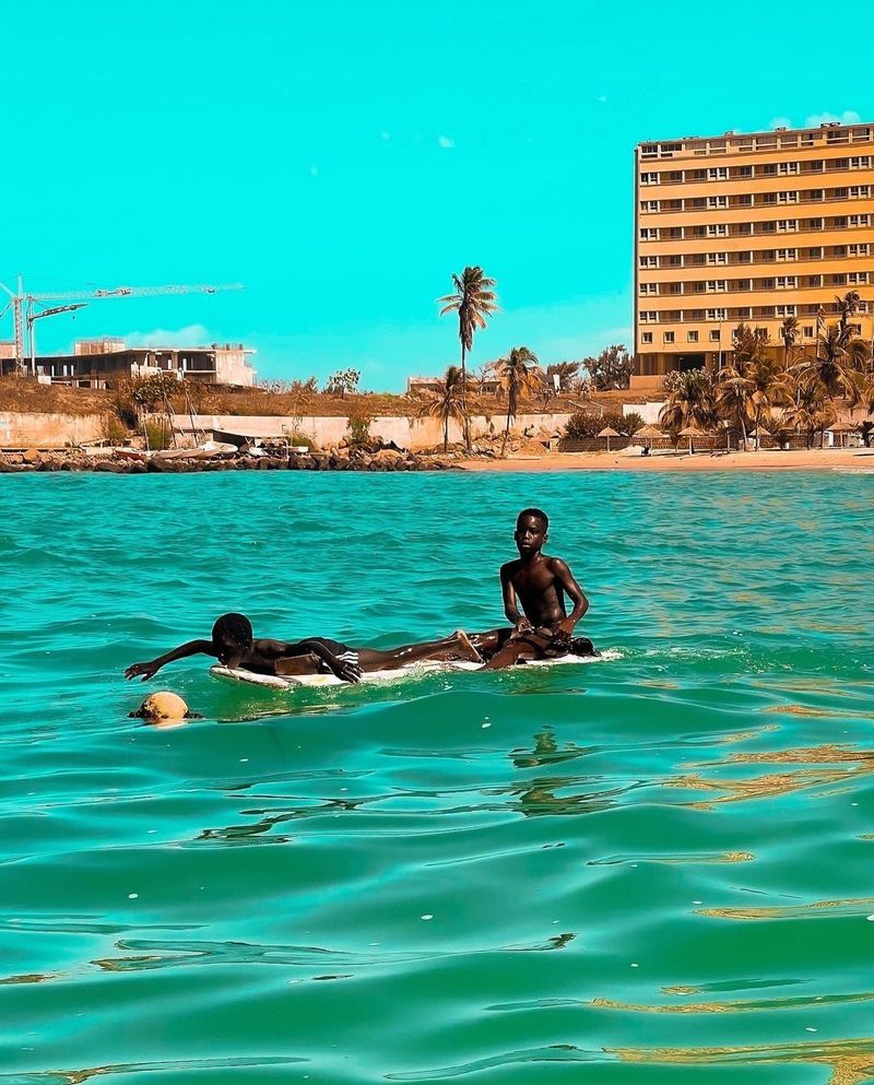 A boy paddles on a board in calm turquoise sea by the city seafront