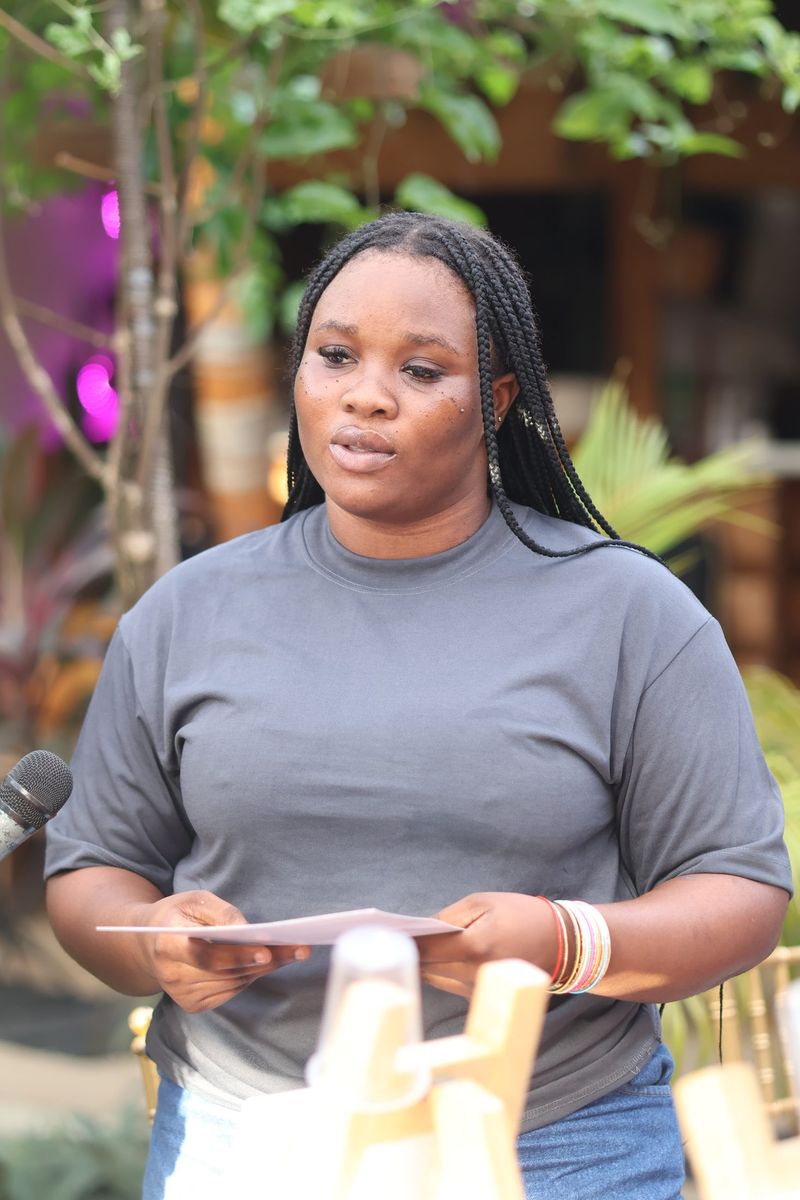 A young woman in a grey top speaks into a microphone while holding a sheet of paper