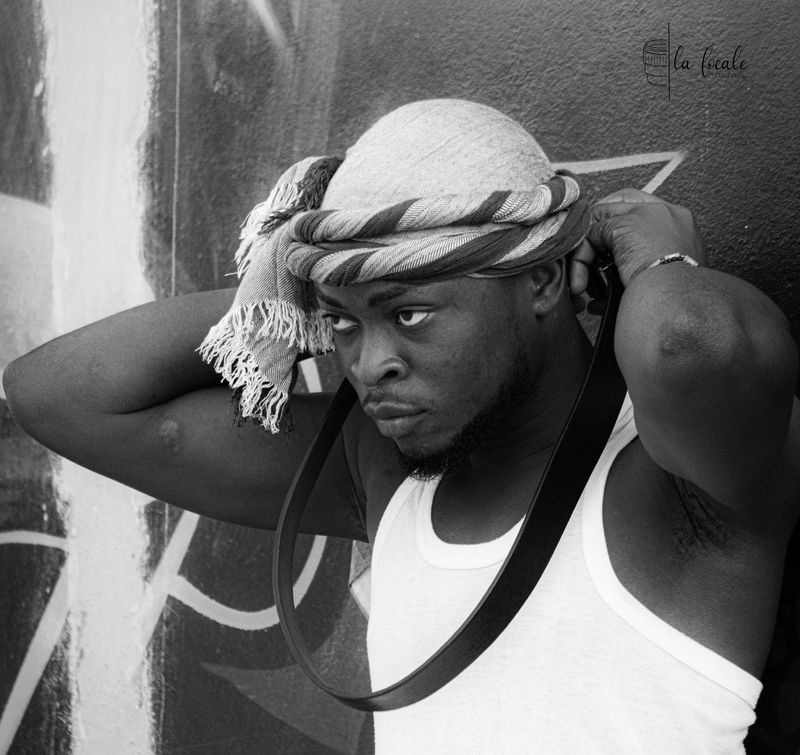 A young man adjusts his head-wrap against a graffiti wall, black and white