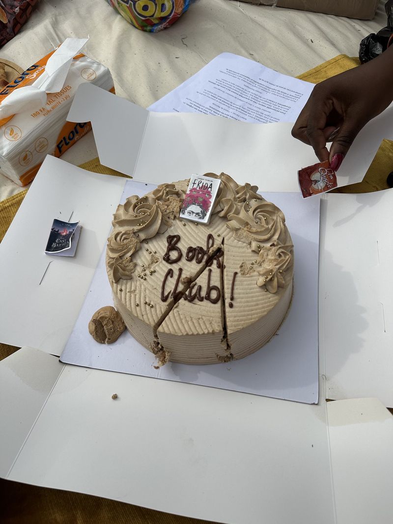 A cream cake iced with the words Book Club beside a printed reading sheet
