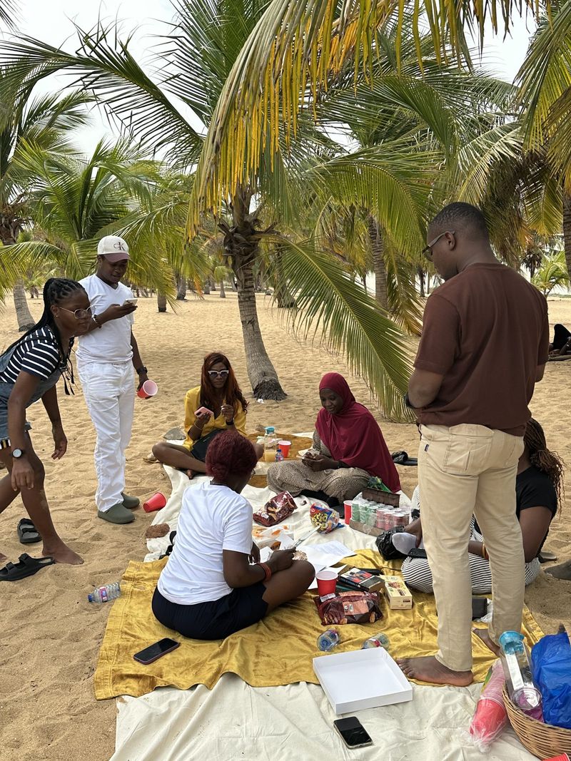 Friends mingle around a beach picnic spread beneath palm trees