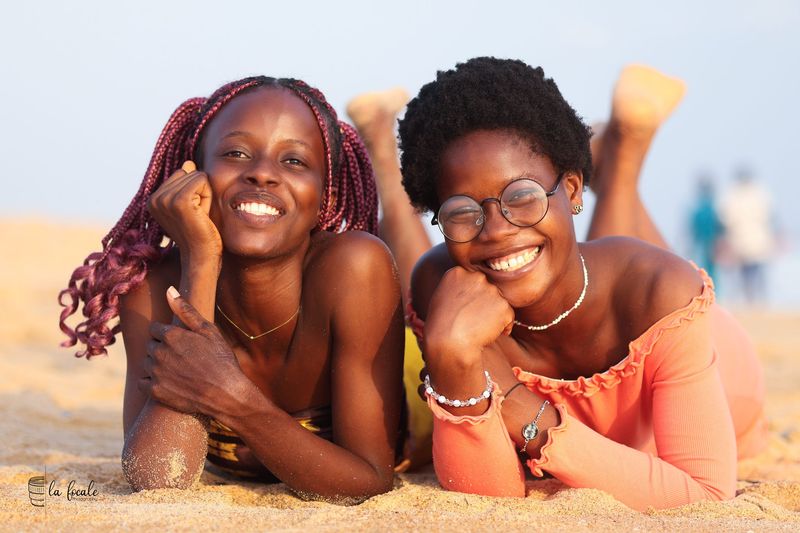 Two young women lie on the sand at the beach, smiling, during a La Focale duo portrait